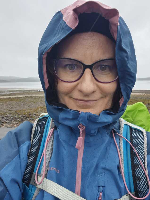 Sonja Warter mit Regenjacke und Kapuze vor einem Strand bei Regenwetter.