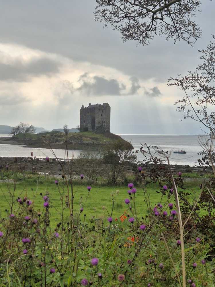 Das auf einer kleinen Insel liegende Castle Stalker bei regnerischer Wolkenstimmung.