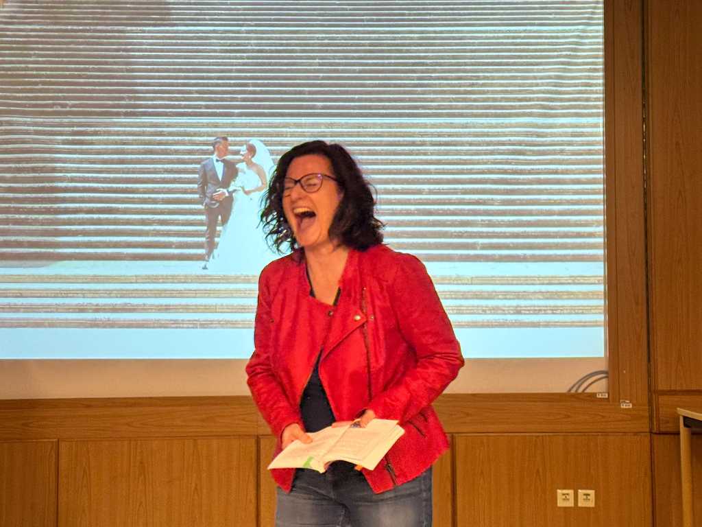 Sonja Warter lacht schallend. Im Hintergrund sieht man ein Bild mit einem Brautpaar.